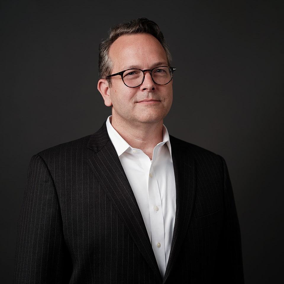 Headshot of Matt Reynolds in a black blazer with a dark background.