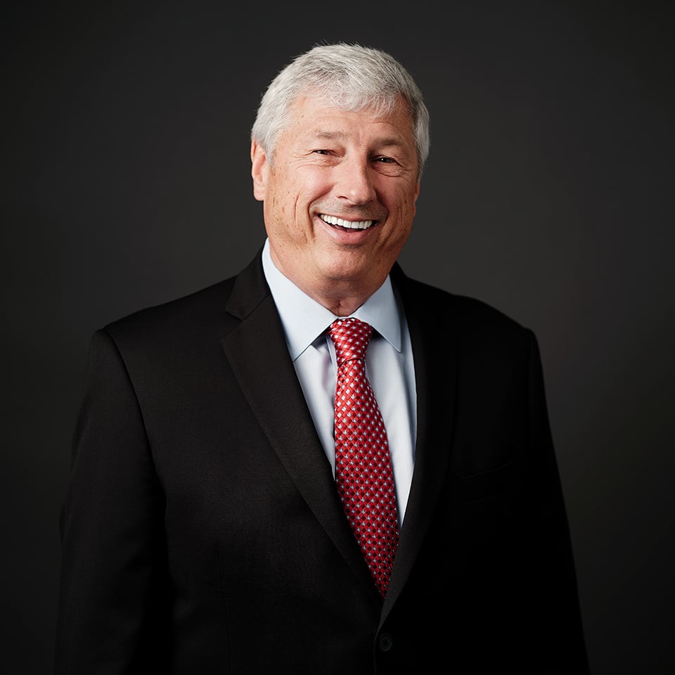 Headshot of James Titak wearing a red tie and black blazer with dark background.