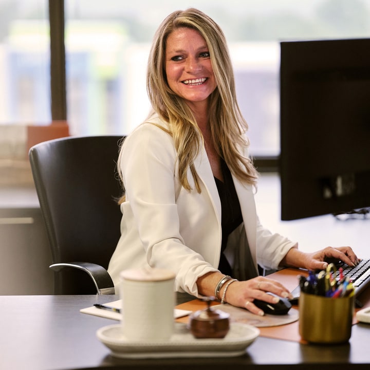 Kelly Raker smiling and sitting at a computer.